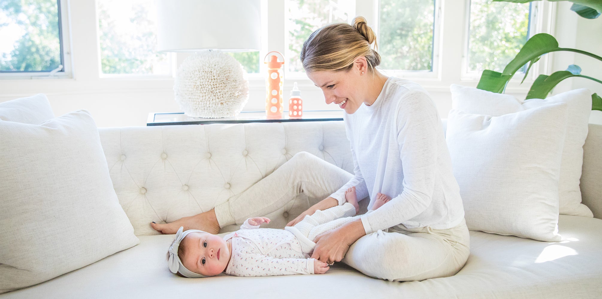 Mother and baby sitting on a couch with Lifefactory glass water bottle and glass baby bottle in the background. 